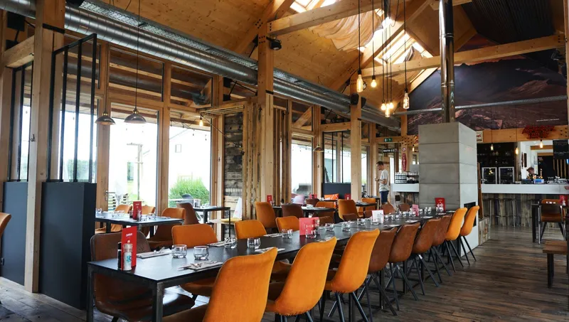 La salle du restaurant, tables dressées et grandes baies vitrées sur la campagne